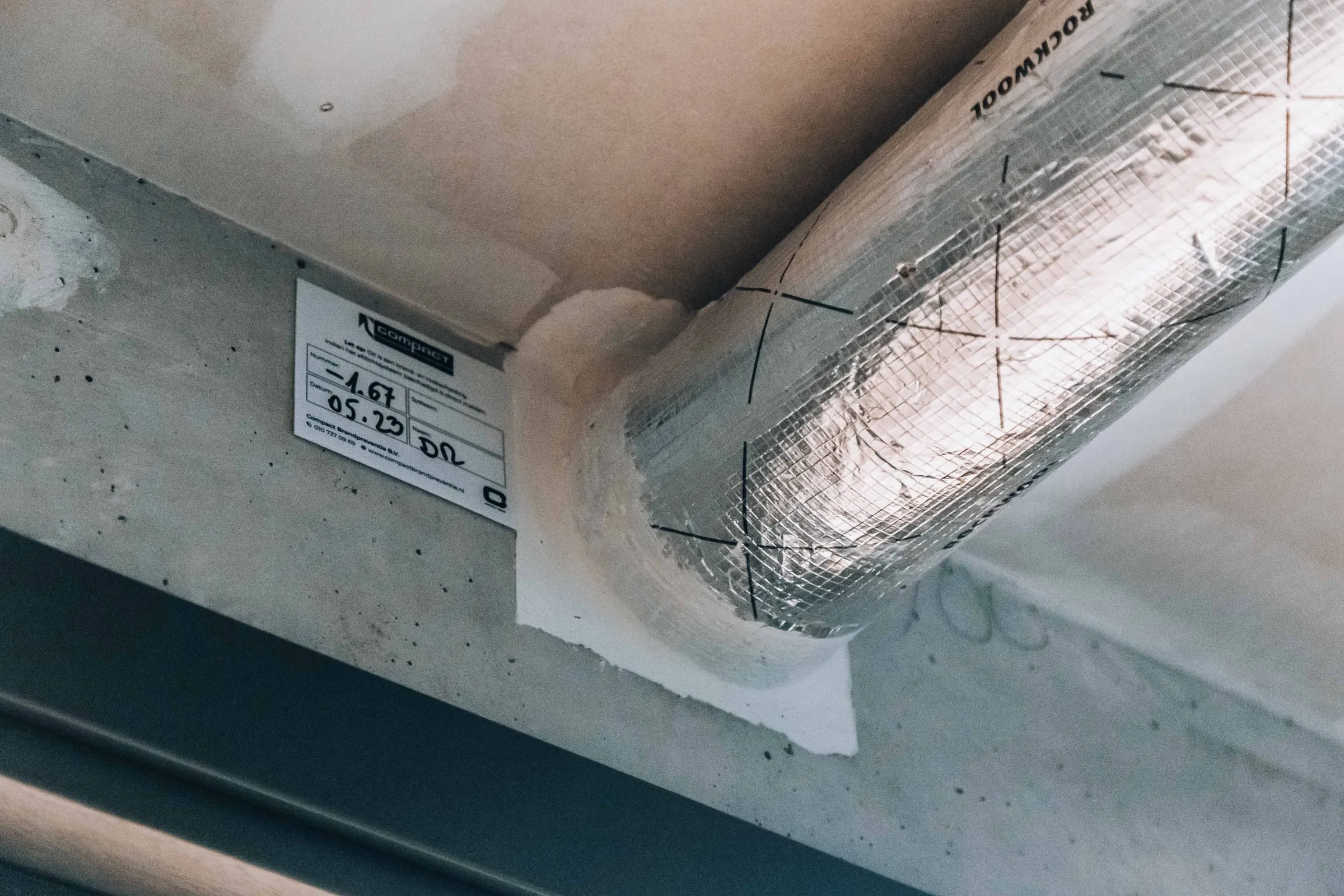 Een afgedichte leiding door een betonwand met het label van Compact ernaast