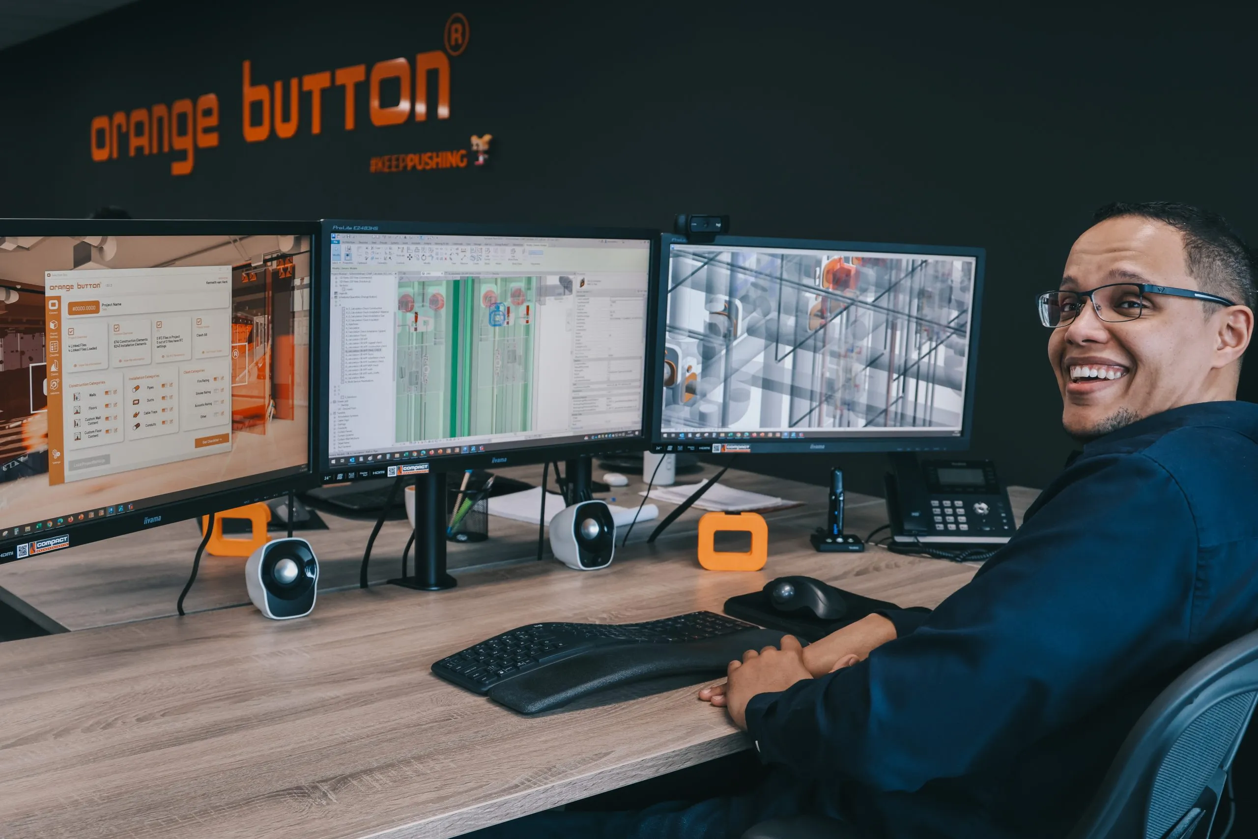 Een BIM-engineer van Compact achter drie schermen met Orange Button en een Revit-model