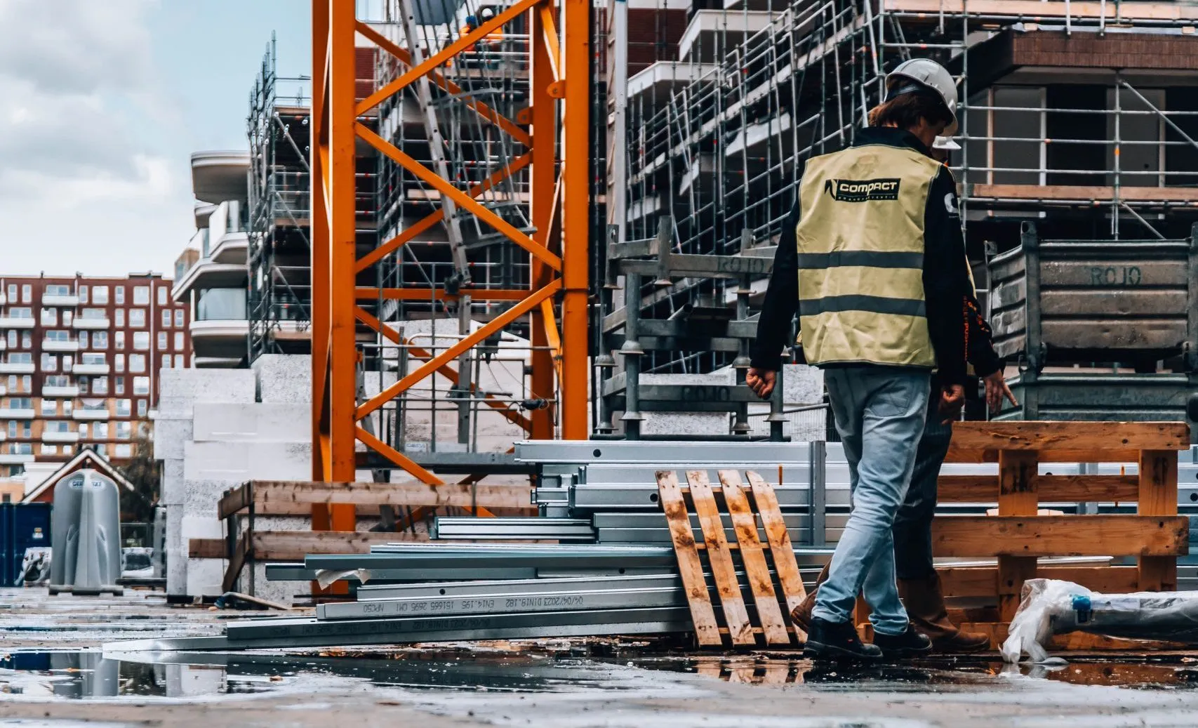 Een monteur van Compact Brandpreventie loopt over een bouwplaats met profielen en een torenkraan