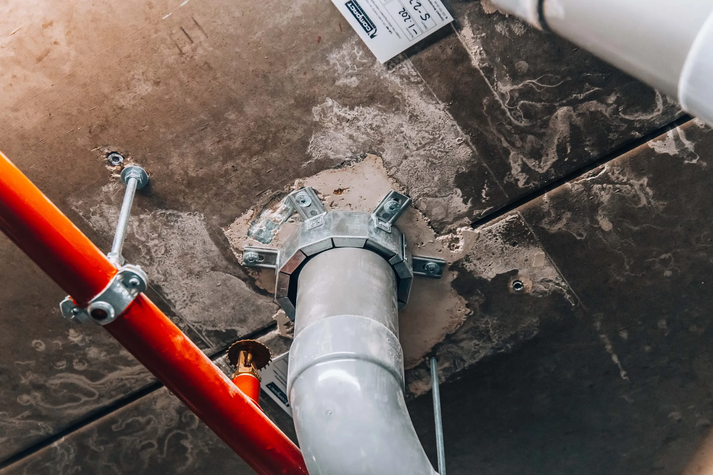 Een brandwerende manchet om een leiding in het plafond, naast een sprinklerleiding