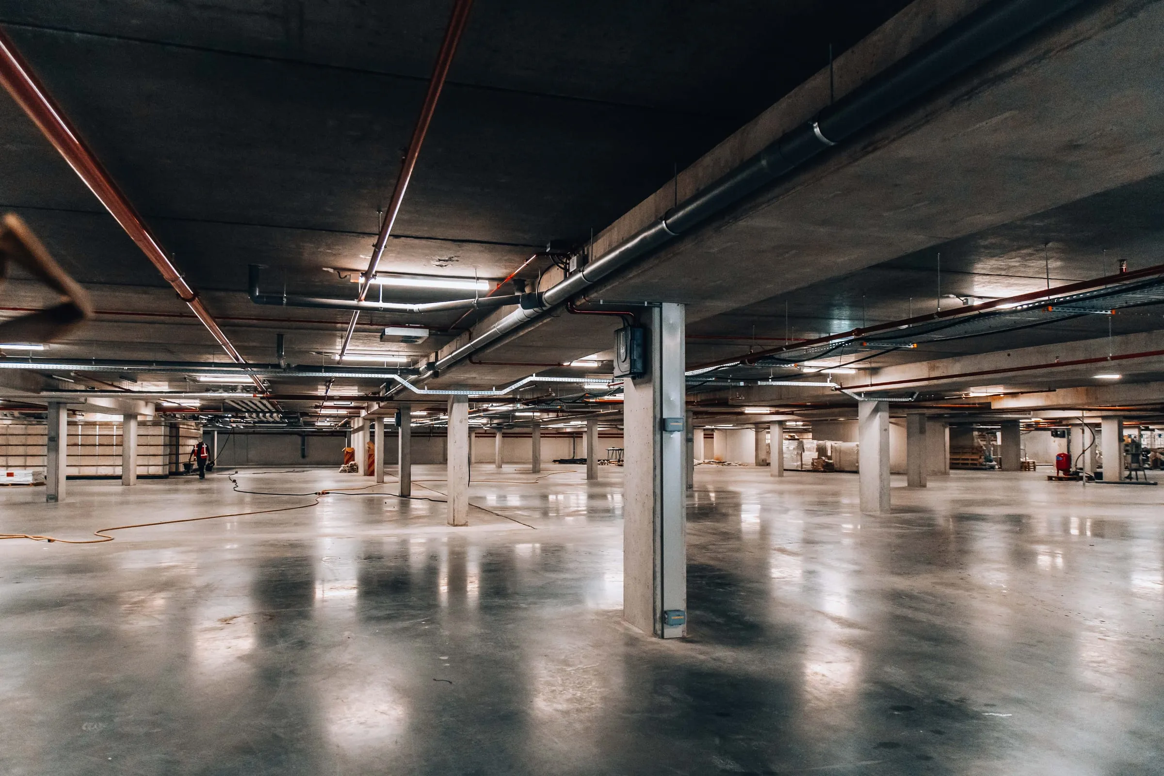 Een opgeleverde parkeergarage met leidingen en kabelgoten aan het plafond